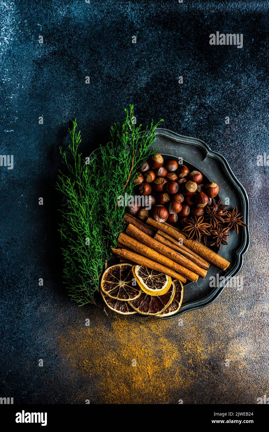 Vue aérienne d'une assiette avec noisettes, bâtons de cannelle, clous de girofle, anis étoilé, oranges séchées et branches de thuja Banque D'Images