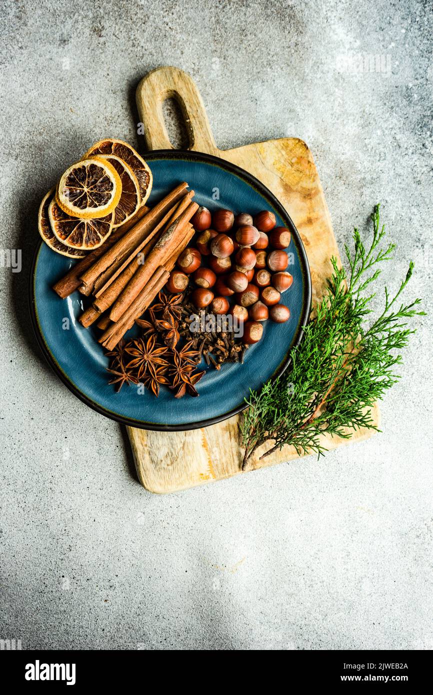 Vue aérienne d'une assiette avec noisettes, bâtons de cannelle, clous de girofle, anis étoilé, oranges séchées et branches de thuja Banque D'Images