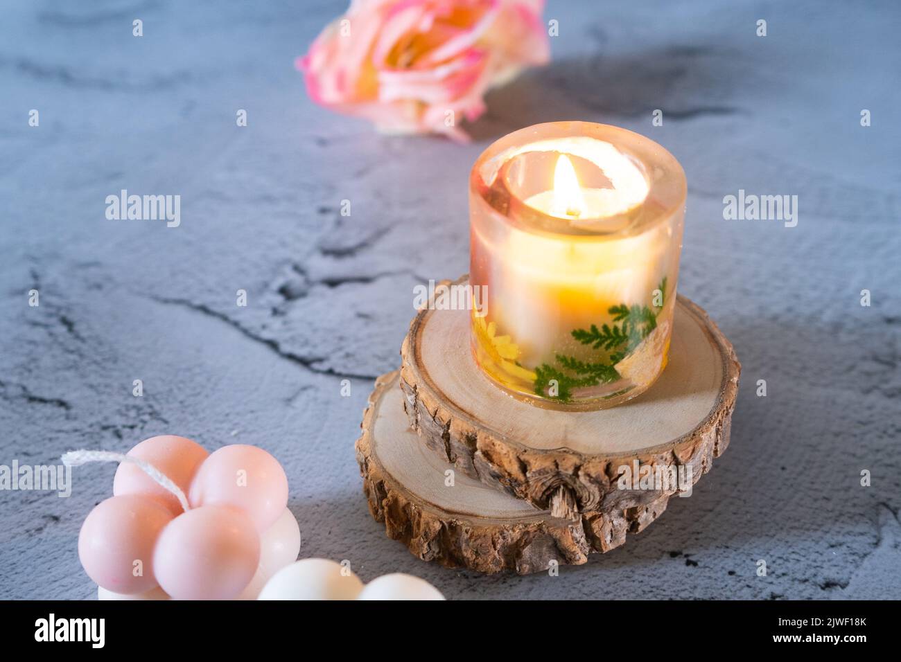 Bougie transparente d'art en résine éclairée sur bois de montagne avec fleurs montrant la décoration de diwali, noël, photo du nouvel an dans des tons pastel Banque D'Images