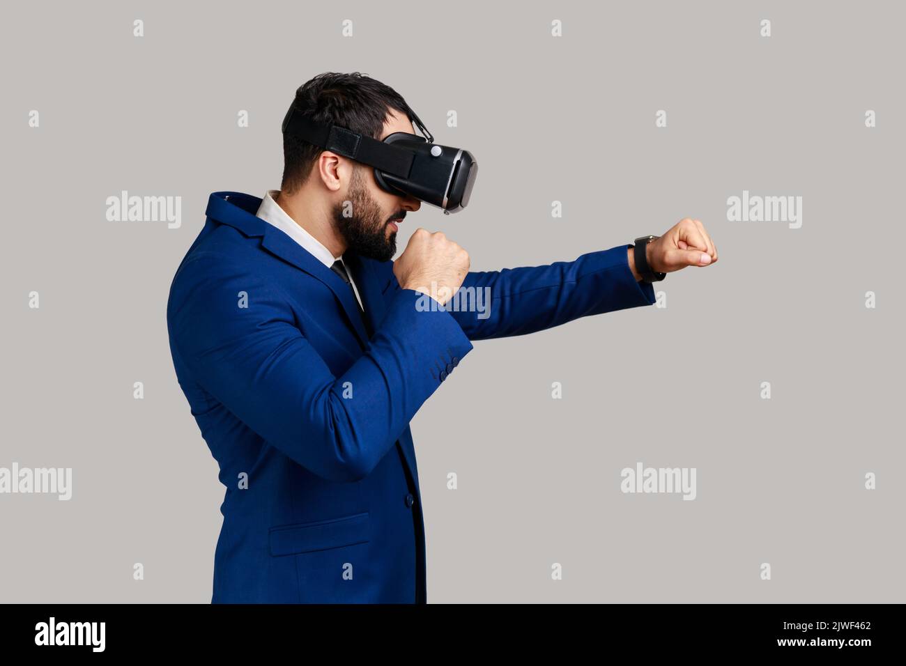 Vue latérale des lunettes de réalité virtuelle MAN sur la tête jouant au jeu de combat, tenant les poings serrés prêts à la boxe, portant un costume de style officiel. Prise de vue en studio isolée sur fond gris. Banque D'Images