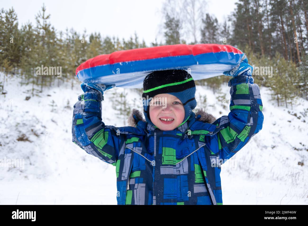 Joyeux garçon actif tenant une tubing gonflable d'hiver au-dessus de sa tête à l'extérieur. Mignon petit enfant heureux avoir du plaisir à l'extérieur en hiver sur le traîneau. Famille Banque D'Images