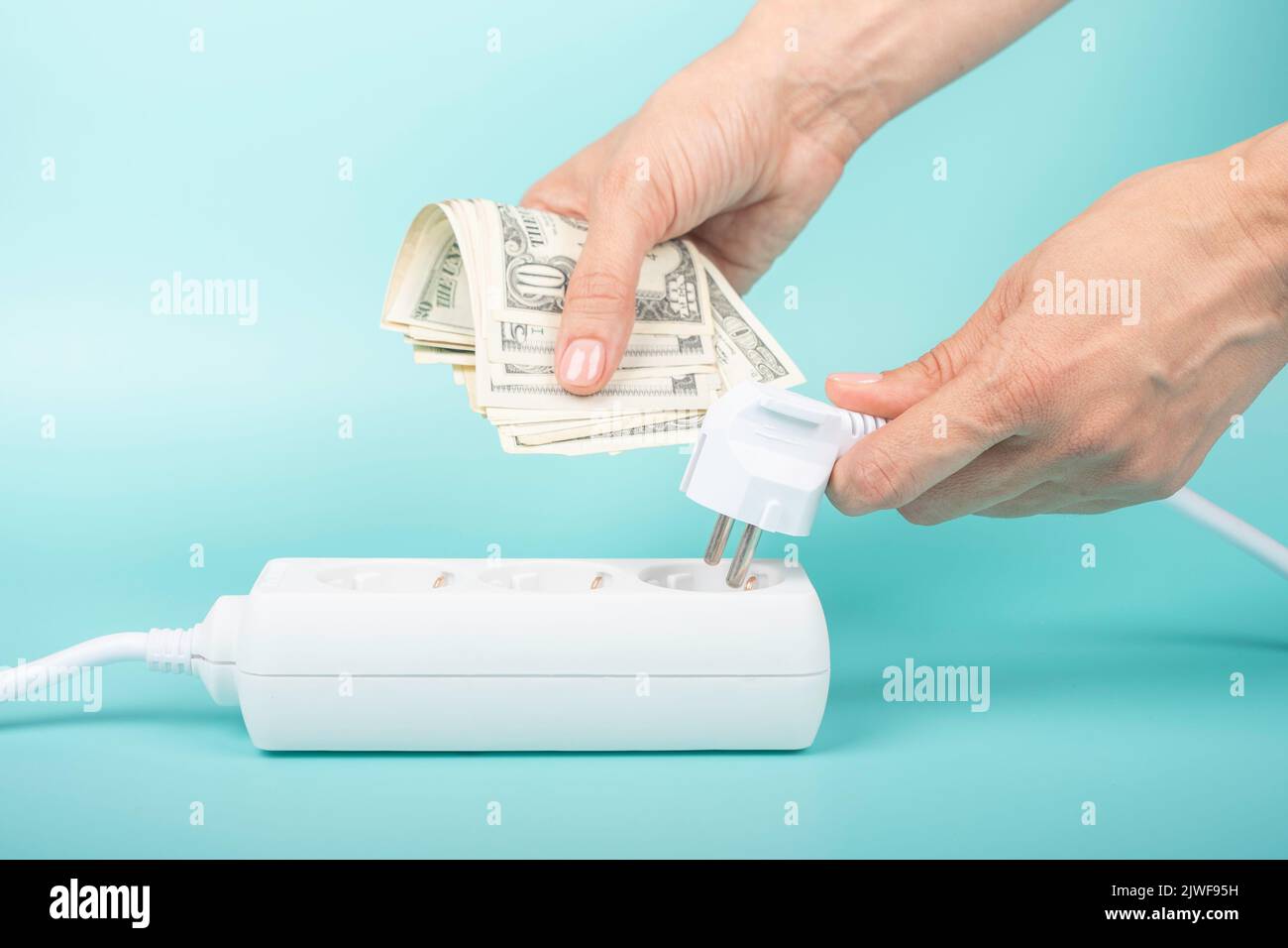 Les mains de la femme tiennent la fiche électrique et les billets en dollars américains près de la rallonge de la barre d'alimentation sur fond bleu. Coût de l'électricité, prix de l'électricité Banque D'Images