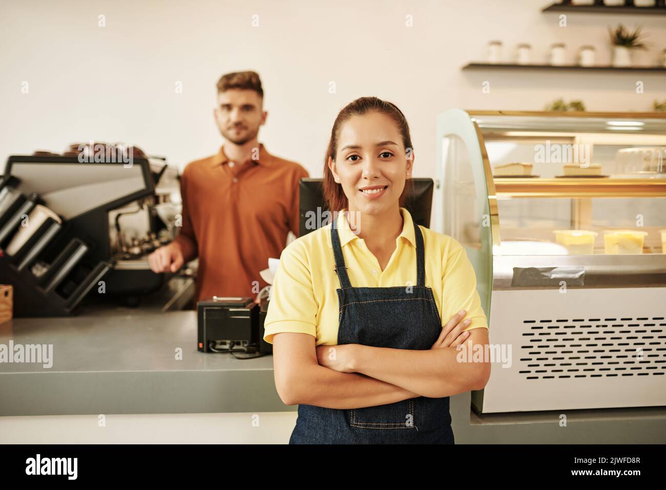 Portrait d'une serveuse de café souriante debout au comptoir avec les bras croisés Banque D'Images