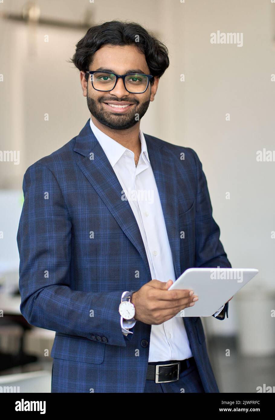 Jeune homme d'affaires indien souriant portant un costume tenant une tablette, vertical. Banque D'Images