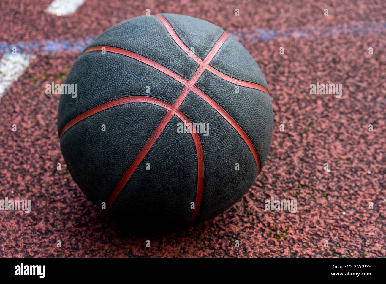 Ballon de basket-ball noir au sol. Gros plan sur le terrain rouge. Basketball dans la rue ou sur un terrain intérieur. Équipement sportif sans personne. Minimalisme. Banque D'Images