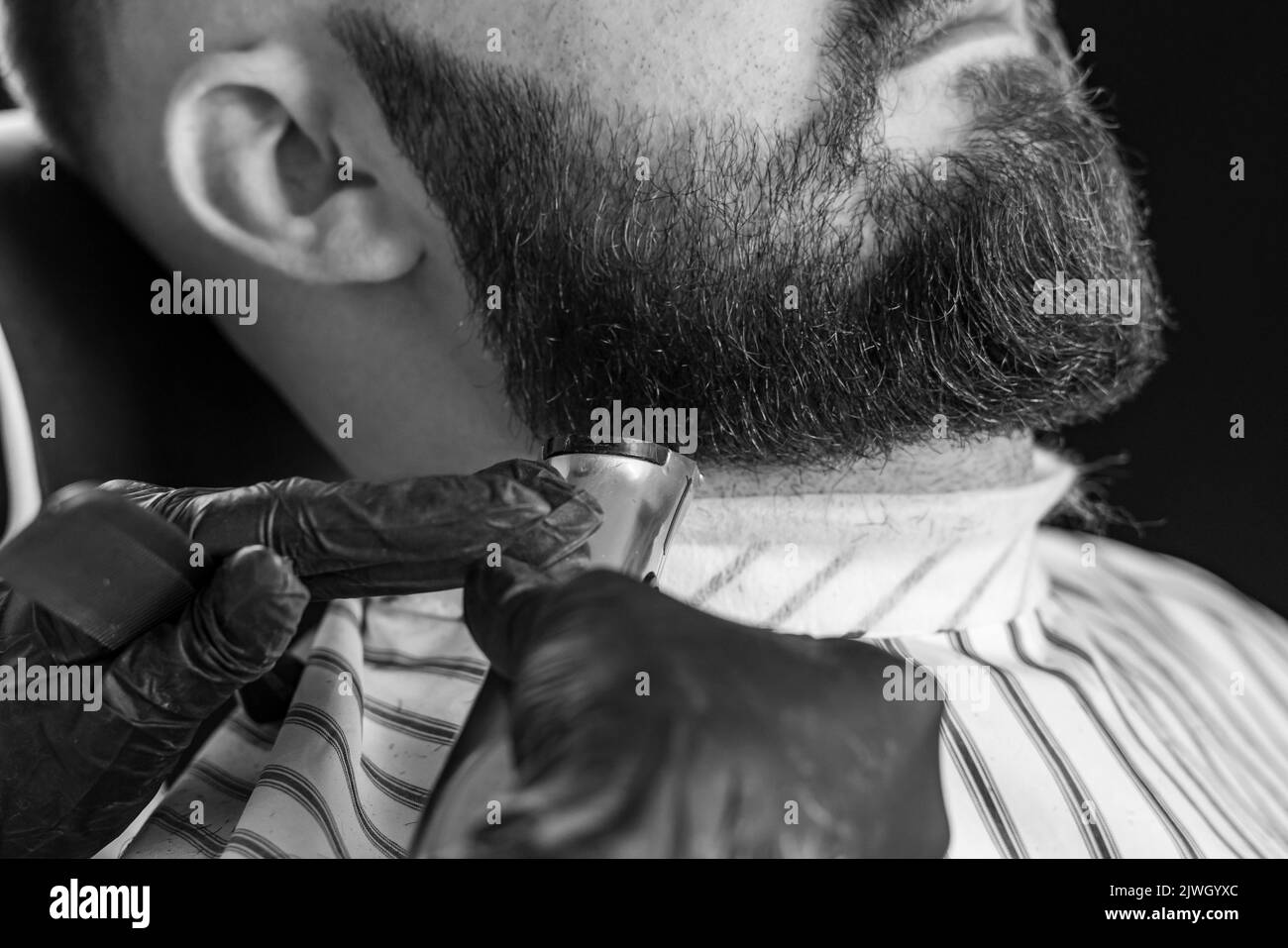 Homme taillé sa barbe avec un rasoir électrique dans un salon de coiffure. Image en noir et blanc. Banque D'Images