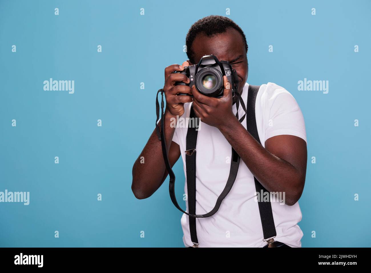 Photographe professionnel plein de confiance ayant un appareil photo reflex numérique pour prendre des photos. Passionné de photographie afro-américain prenant des photos sur fond bleu. Prise de vue en studio Banque D'Images