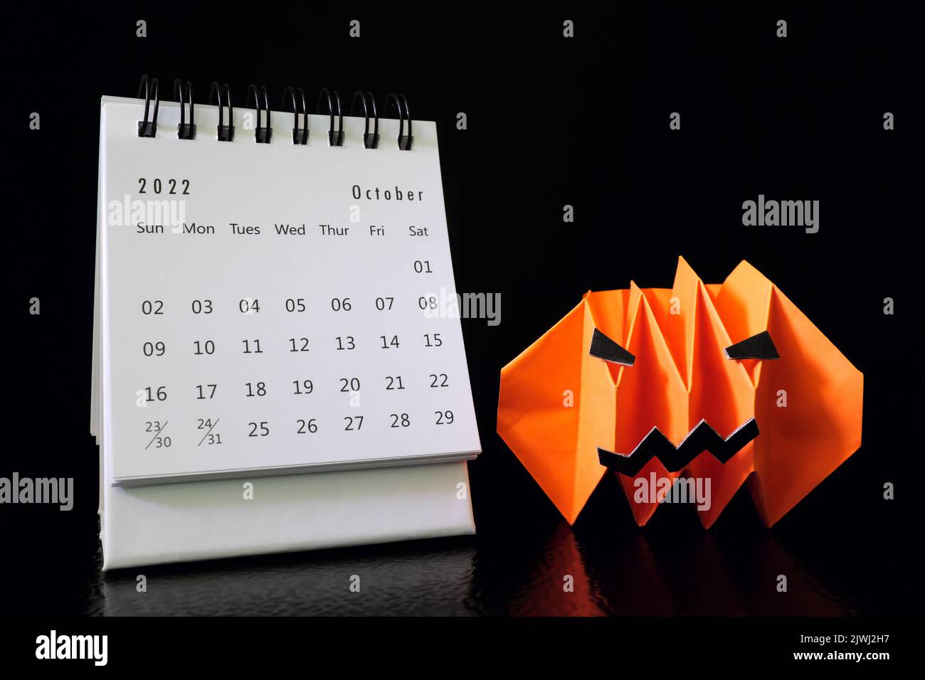 Bonjour octobre 2022 avec Halloween concept. Calendrier de bureau avec papier artisanal à motif citrouille ou citrouille ou lanterne sur fond noir foncé. Banque D'Images