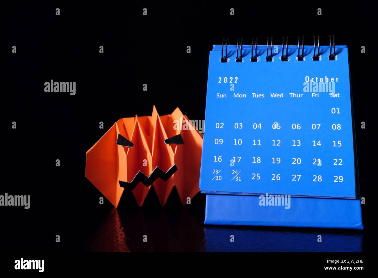 Bonjour octobre 2022 avec Halloween concept. Calendrier de bureau avec papier artisanal à motif citrouille ou citrouille ou lanterne sur fond noir foncé. Banque D'Images