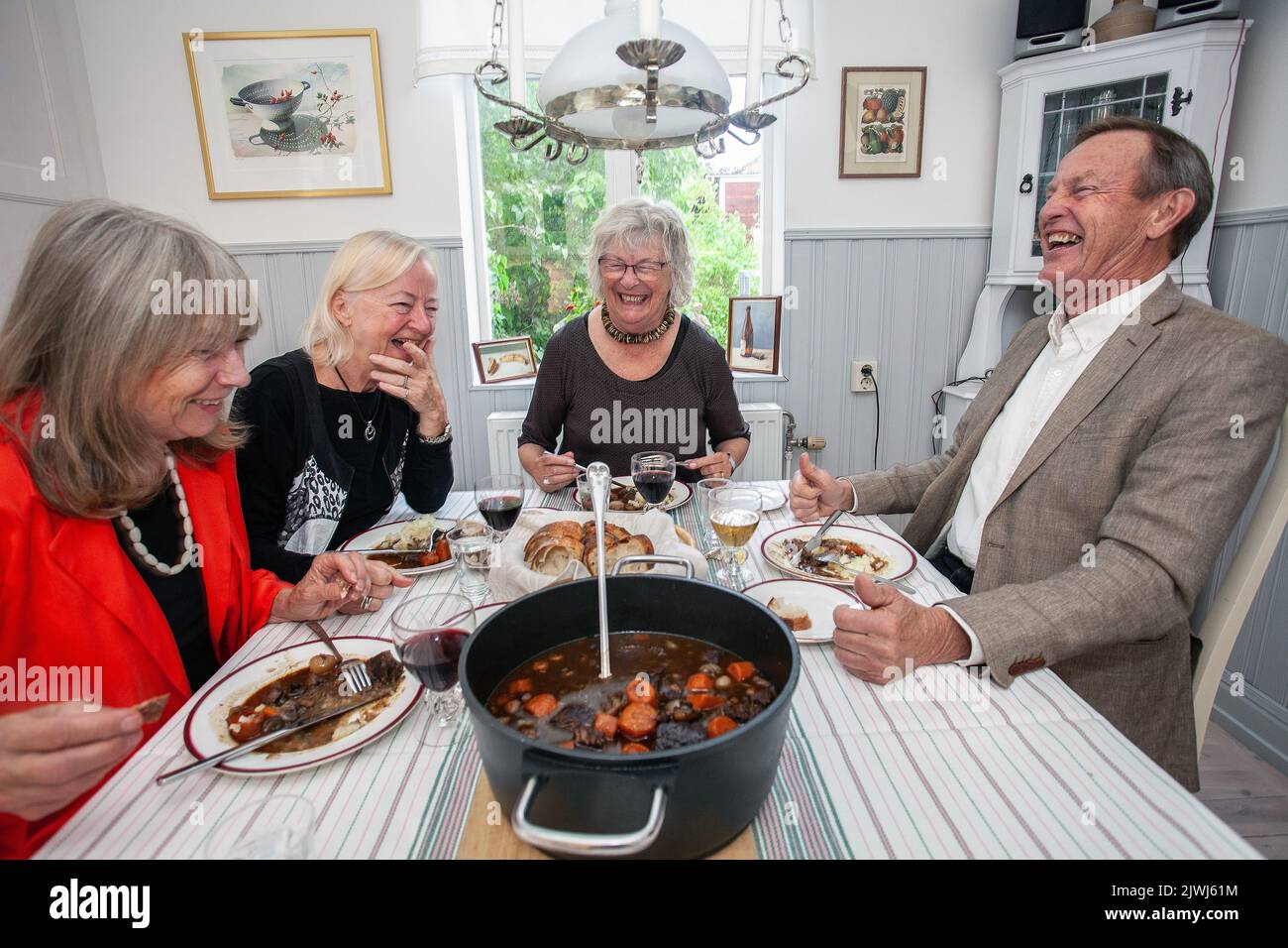 Groupe de personnes ayant dîner à la maison. Des amis heureux assis autour de la table à manger manger de la nourriture et de parler Banque D'Images
