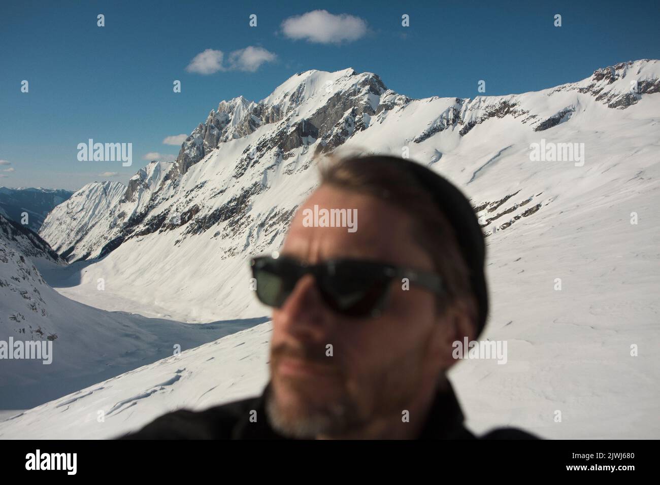 Homme dans des lunettes de soleil sur une montagne ensoleillée et enneigée, Selkirk Mountains, Canada Banque D'Images