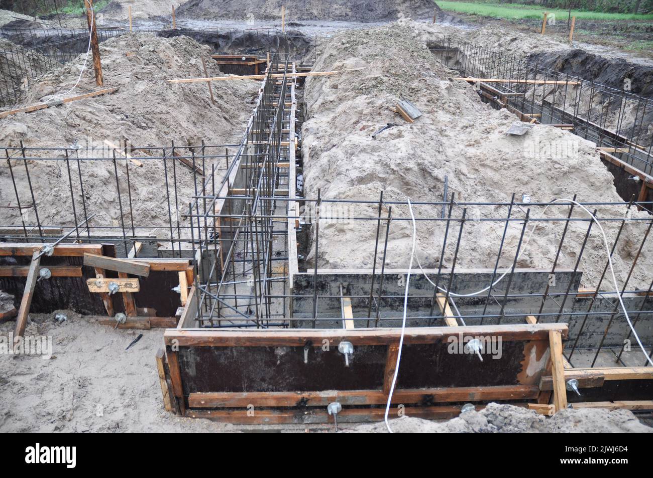 Semelle en bande, construction de fondations. Un gros plan d'une fondation de maison de bande avec une tranchée creusée, cadre en bois et filet de renforcement installé, prêt f Banque D'Images