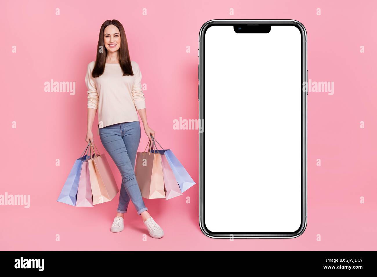 Photo pleine longueur de la femme fashionista avec des paquets de boutique présentant grand téléphone écran tactile nouvelle interface isolé couleur rose fond Banque D'Images