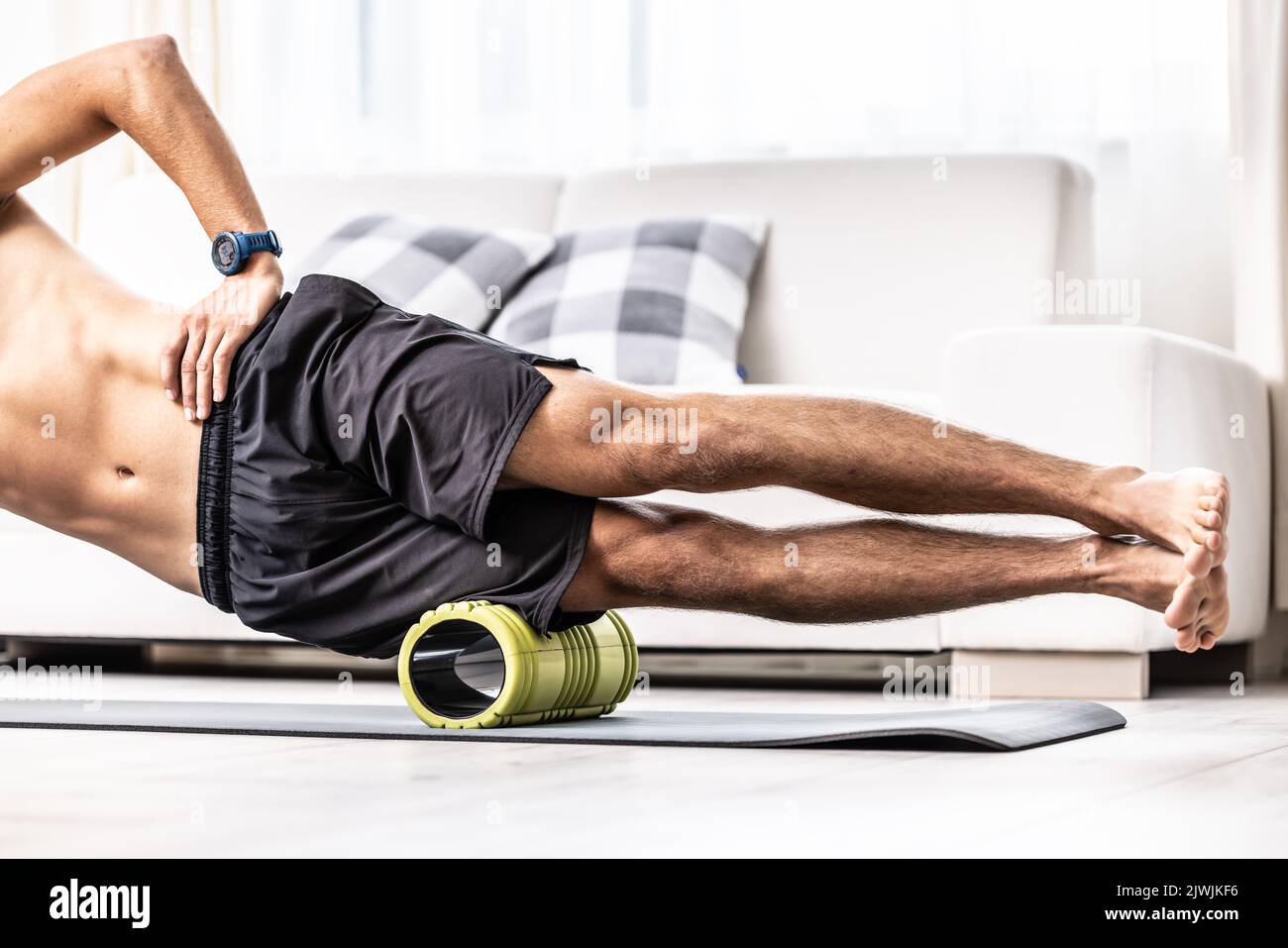 Jeune homme massant le muscle latéral de la cuisse avec rouleau en mousse. Banque D'Images