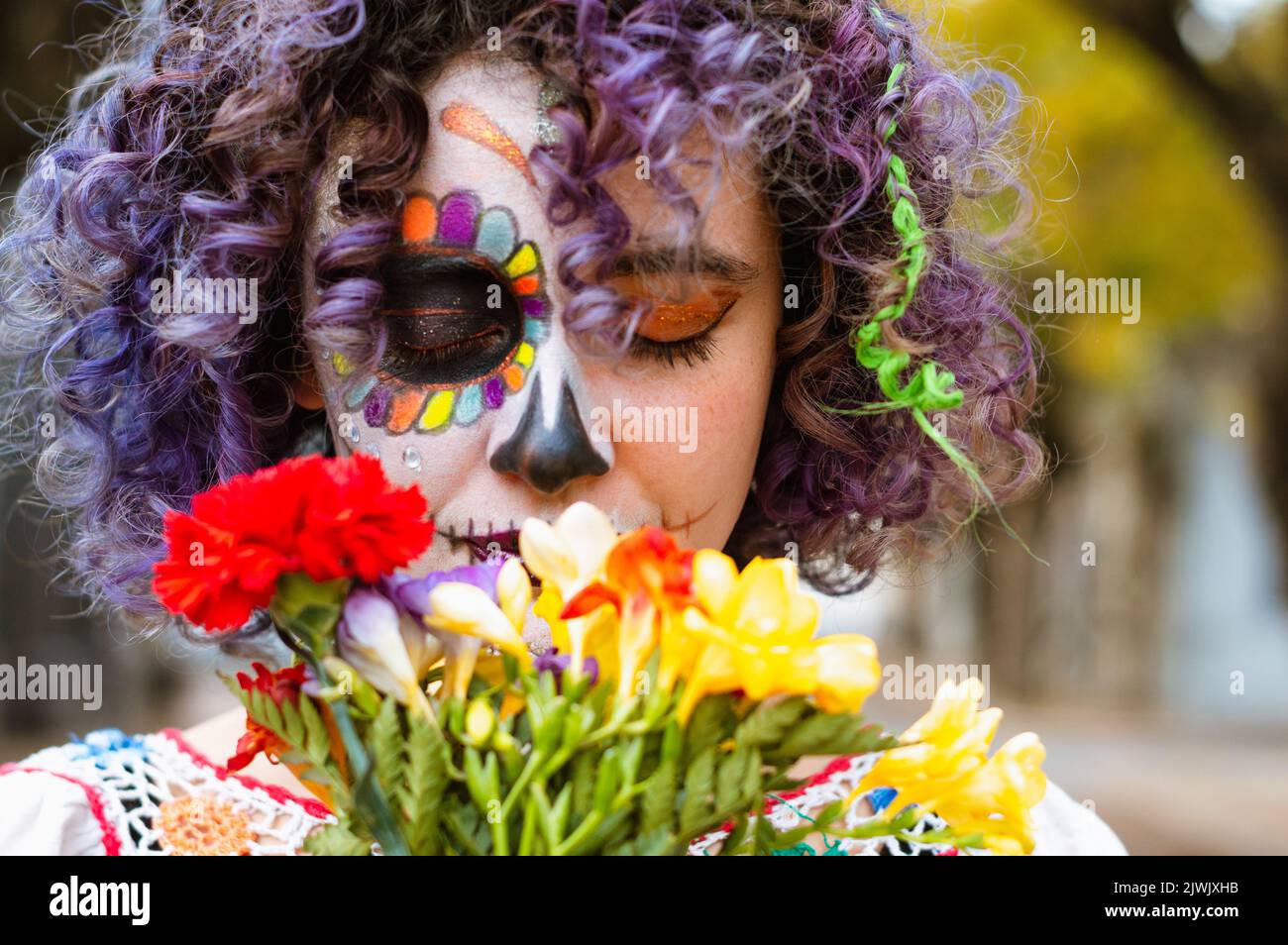 gros plan et vue de face portrait de la jeune femme caucasienne avec la Calavera catrina maquillage avec les yeux fermés et odeur des fleurs à l'extérieur Banque D'Images