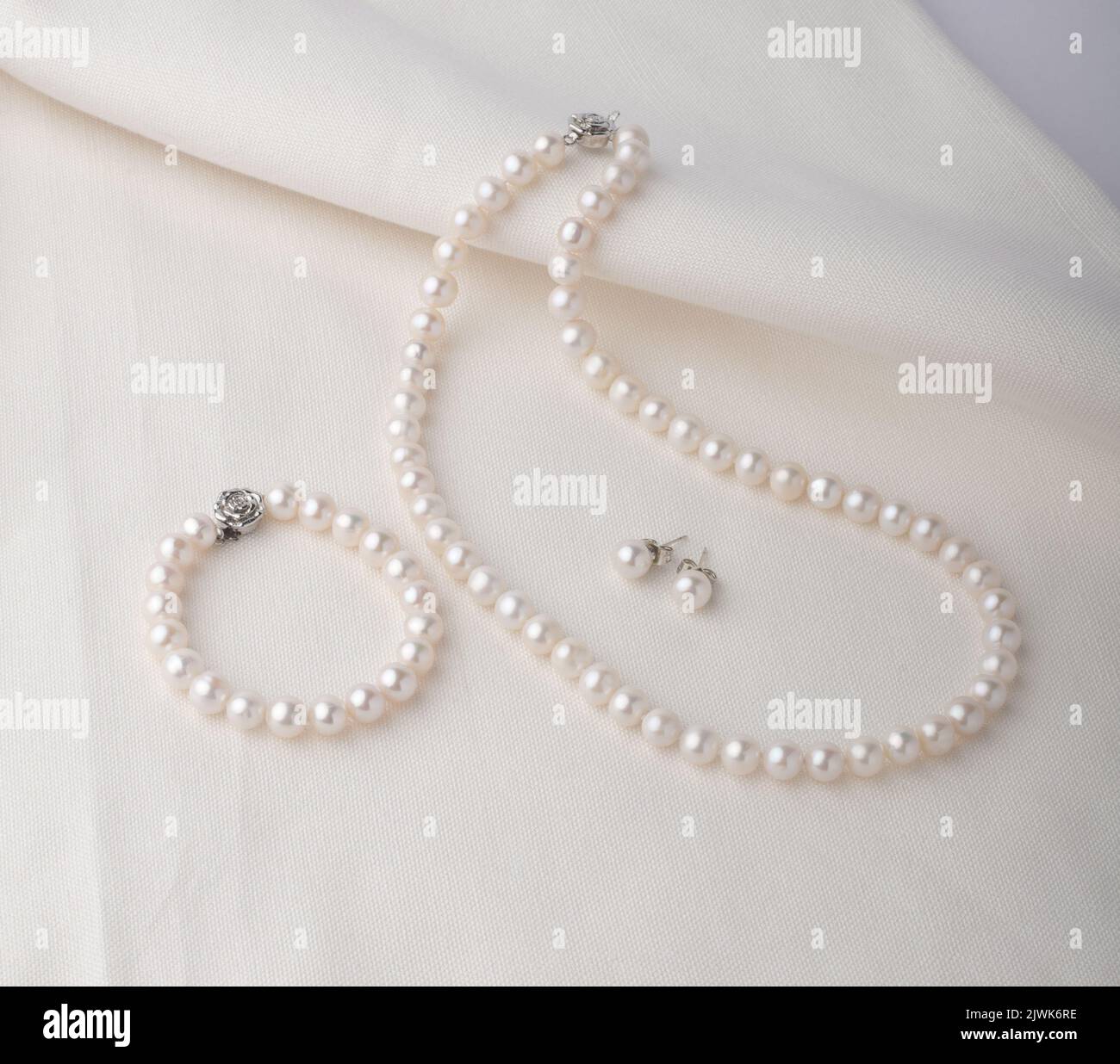 Ensemble de bijoux en perles, beau bracelet, boucles d'oreilles et collier sur tissu blanc Banque D'Images