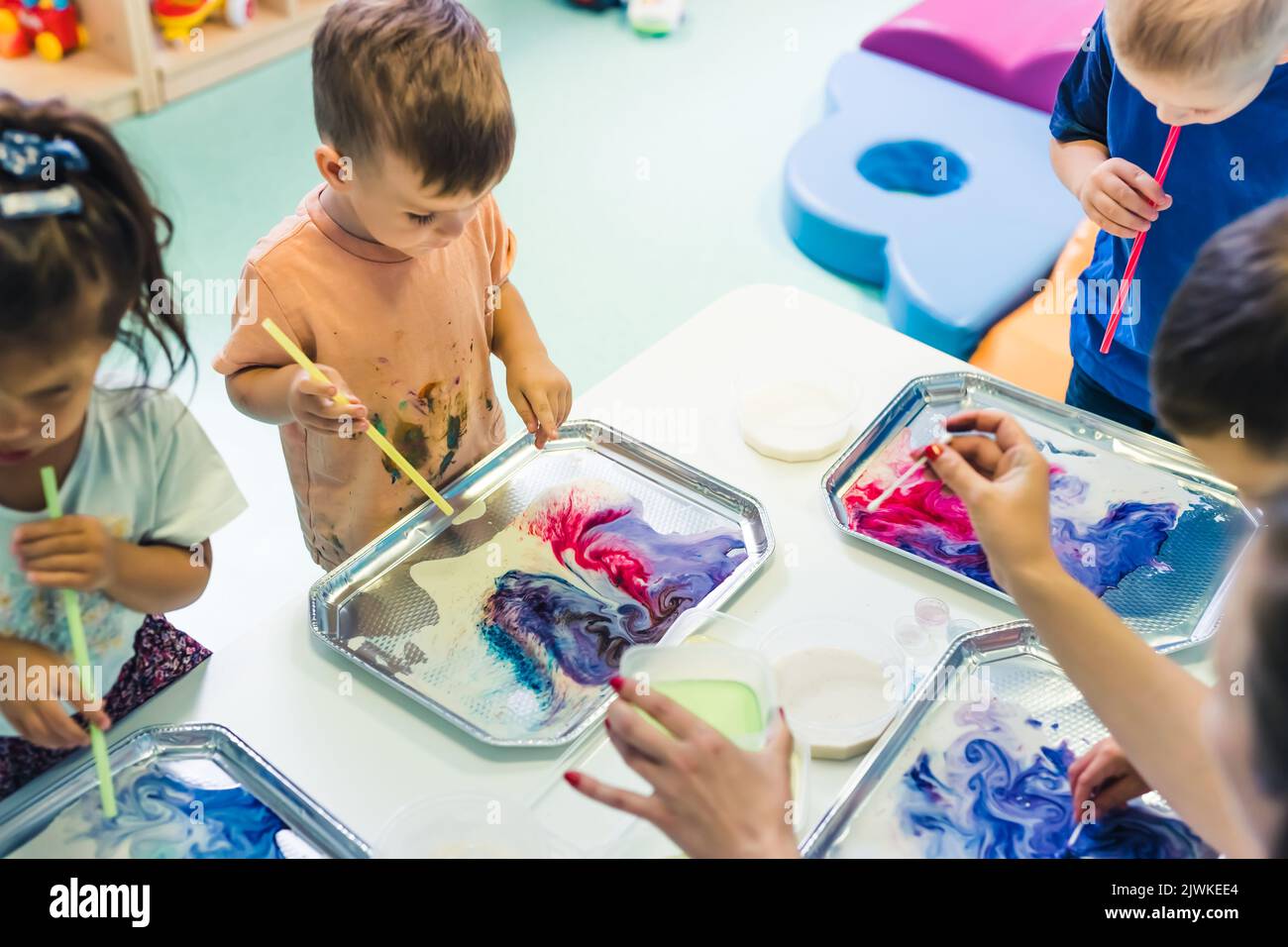 École maternelle multiculturelle. Les tout-petits jouant avec des pailles rayées et la peinture au lait, en utilisant des colorants alimentaires non toxiques pour les couleurs. Activité créative des enfants pour utiliser leurs sens et le développement du cerveau. Peinture au doigt. Photo de haute qualité Banque D'Images