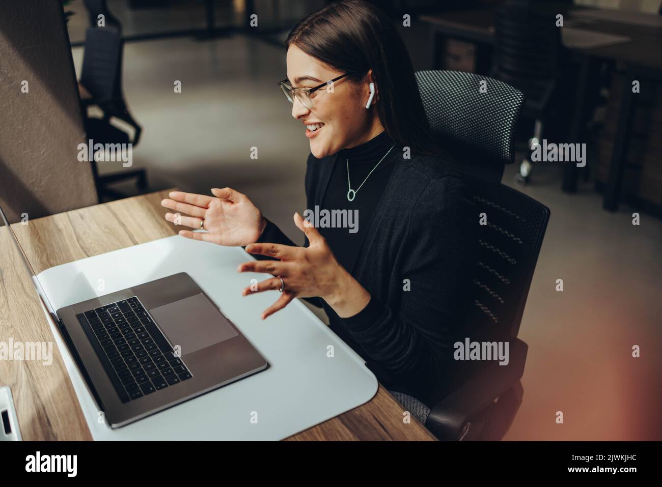 femme d'affaires parlant lors d'une réunion en ligne dans un bureau de co-working moderne. Heureuse entrepreneure communiquant avec ses associés wh Banque D'Images