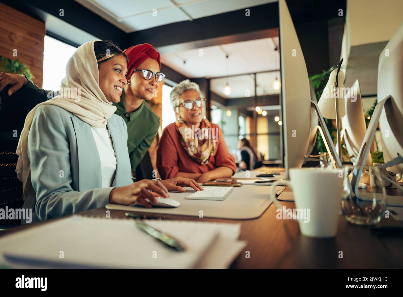Des femmes d'affaires heureuses ayant une discussion tout en regardant un écran d'ordinateur dans un bureau. Femmes d'affaires multiculturelles travaillant en équipe dans un co- Banque D'Images