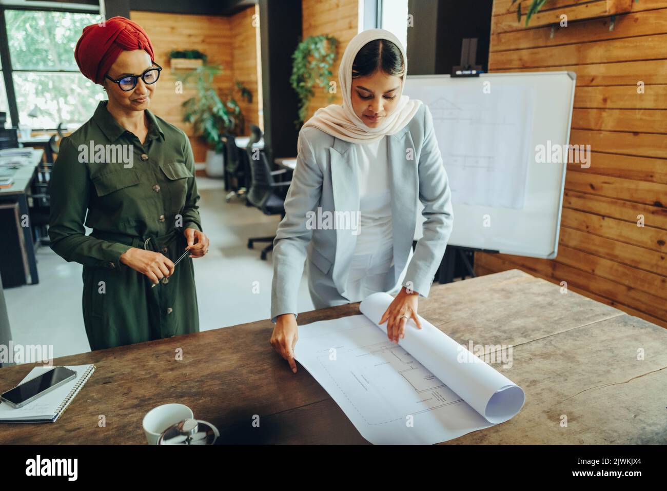 Deux architectes musulmans travaillant avec des plans-plans dans un bureau moderne. Deux femmes d'affaires créatives planifiant un projet novateur. Femmes designers Banque D'Images