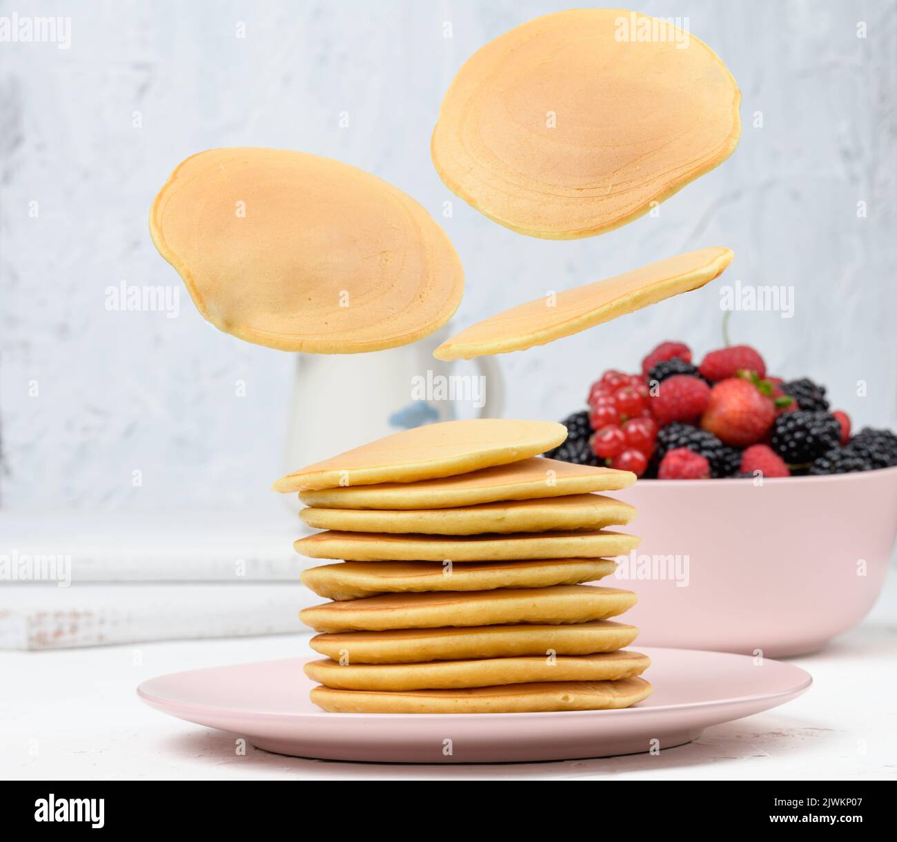 Une pile de crêpes cuites avec des fruits dans une assiette ronde sur une table blanche Banque D'Images