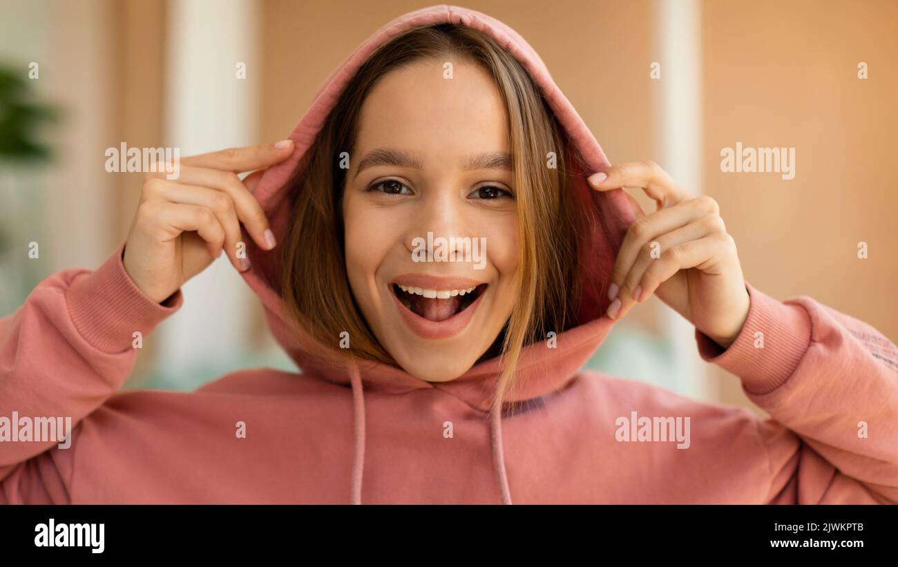 Portrait d'une jeune fille excitée portant une capuche et souriant à l'appareil photo, posant à l'intérieur à l'intérieur de la maison Banque D'Images