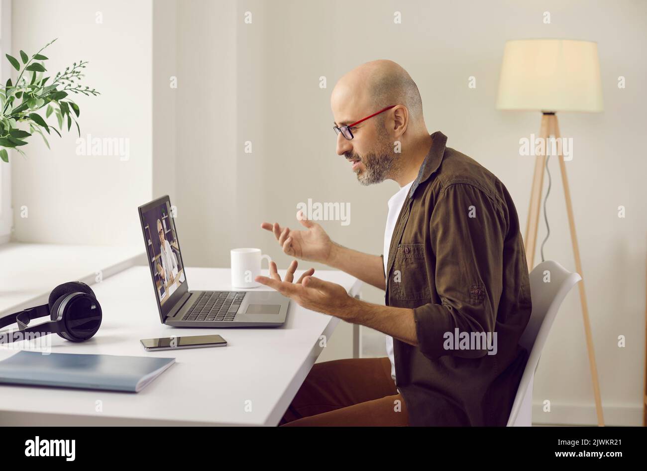 Homme assis à un bureau à domicile et ayant une réunion d'affaires en ligne sur un ordinateur portable Banque D'Images