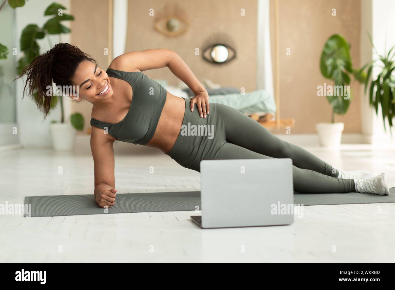 FIT afro-américaine femme debout sur le côté de la planche sur le tapis de yoga, formation avec ordinateur portable à la maison Banque D'Images