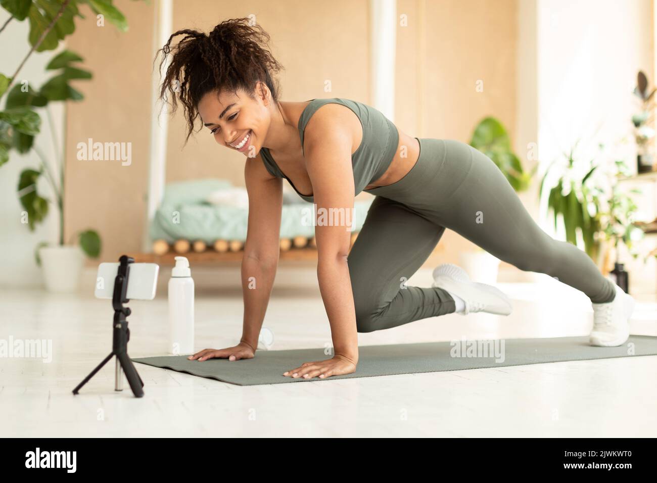 Entraînement en ligne. FIT afro-américaine femme faisant des alpinistes exercice sur le tapis de yoga, regardant le smartphone Banque D'Images