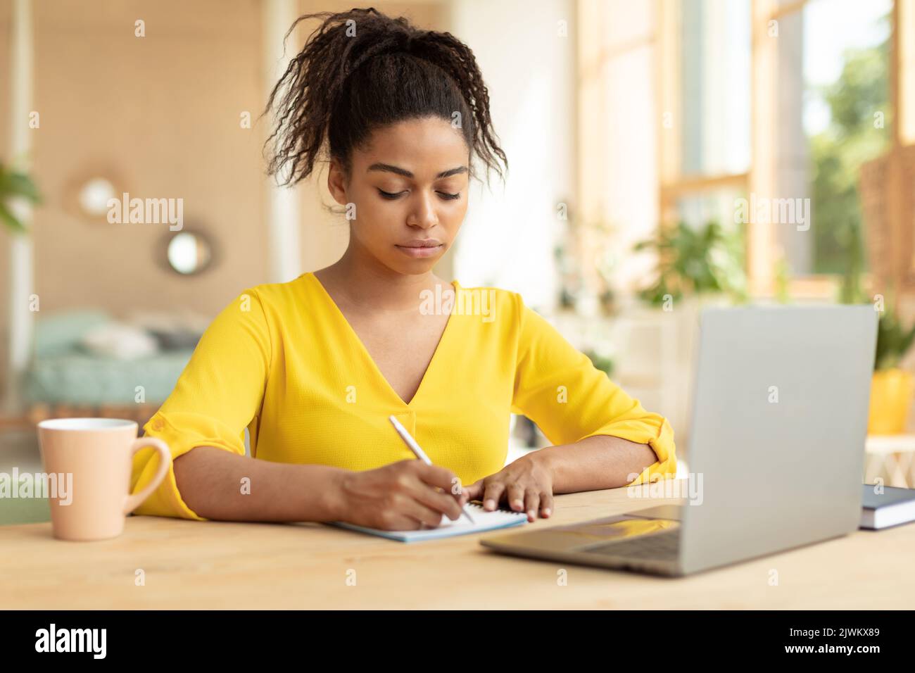 Une étudiante noire ciblée prend des notes, regarde des cours en ligne sur un ordinateur portable, apprend en ligne à la maison, s'assoit au bureau Banque D'Images