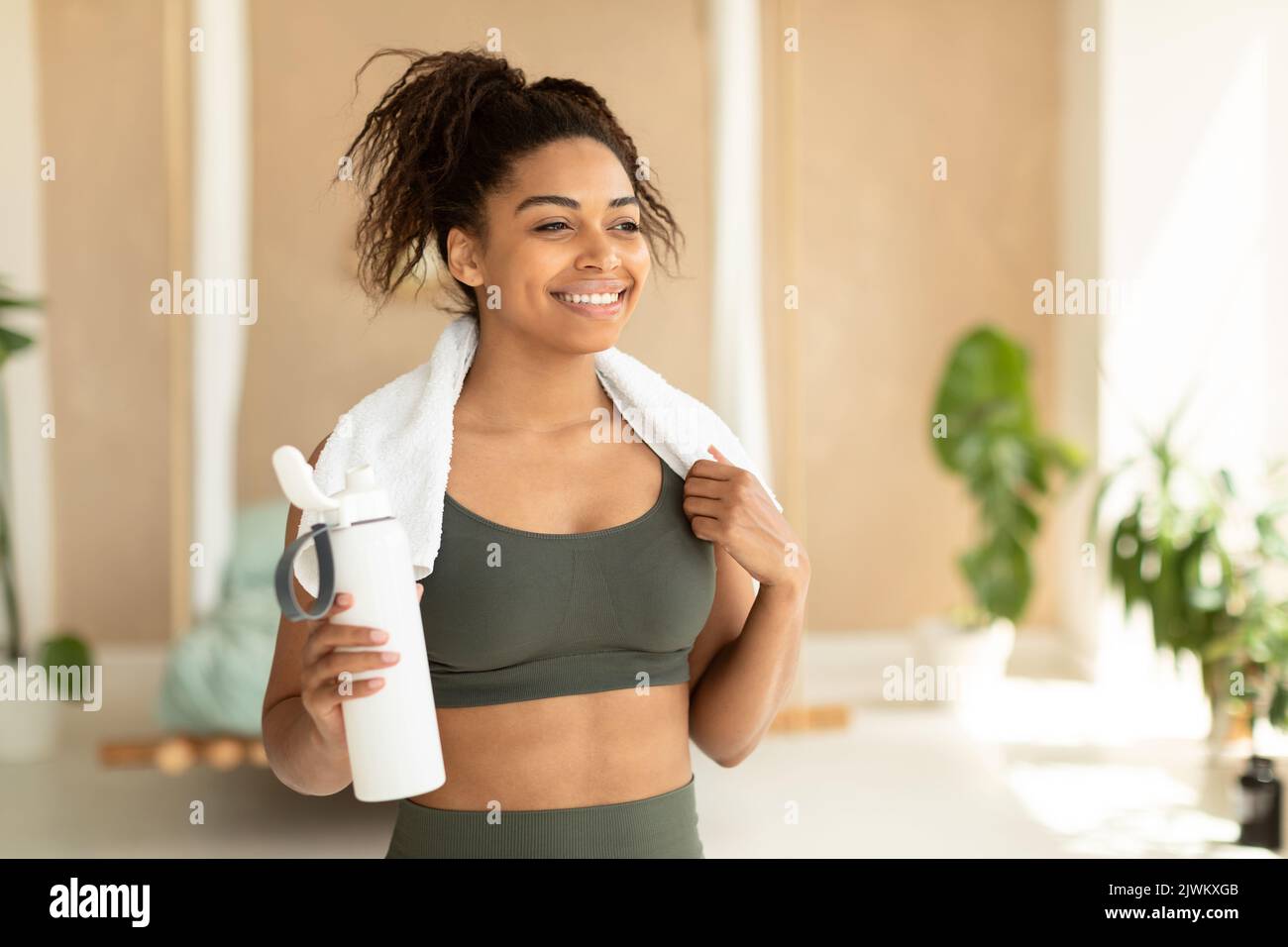 Portrait d'une femme noire heureuse en vêtements de sport et serviette blanche sur le cou tenant une bouteille avec de l'eau douce, espace copie Banque D'Images