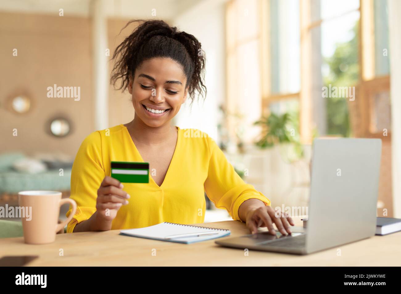 Effectuer une transaction financière. Femme noire excitée tenant une carte de crédit et utilisant un ordinateur personnel, assis à un bureau Banque D'Images