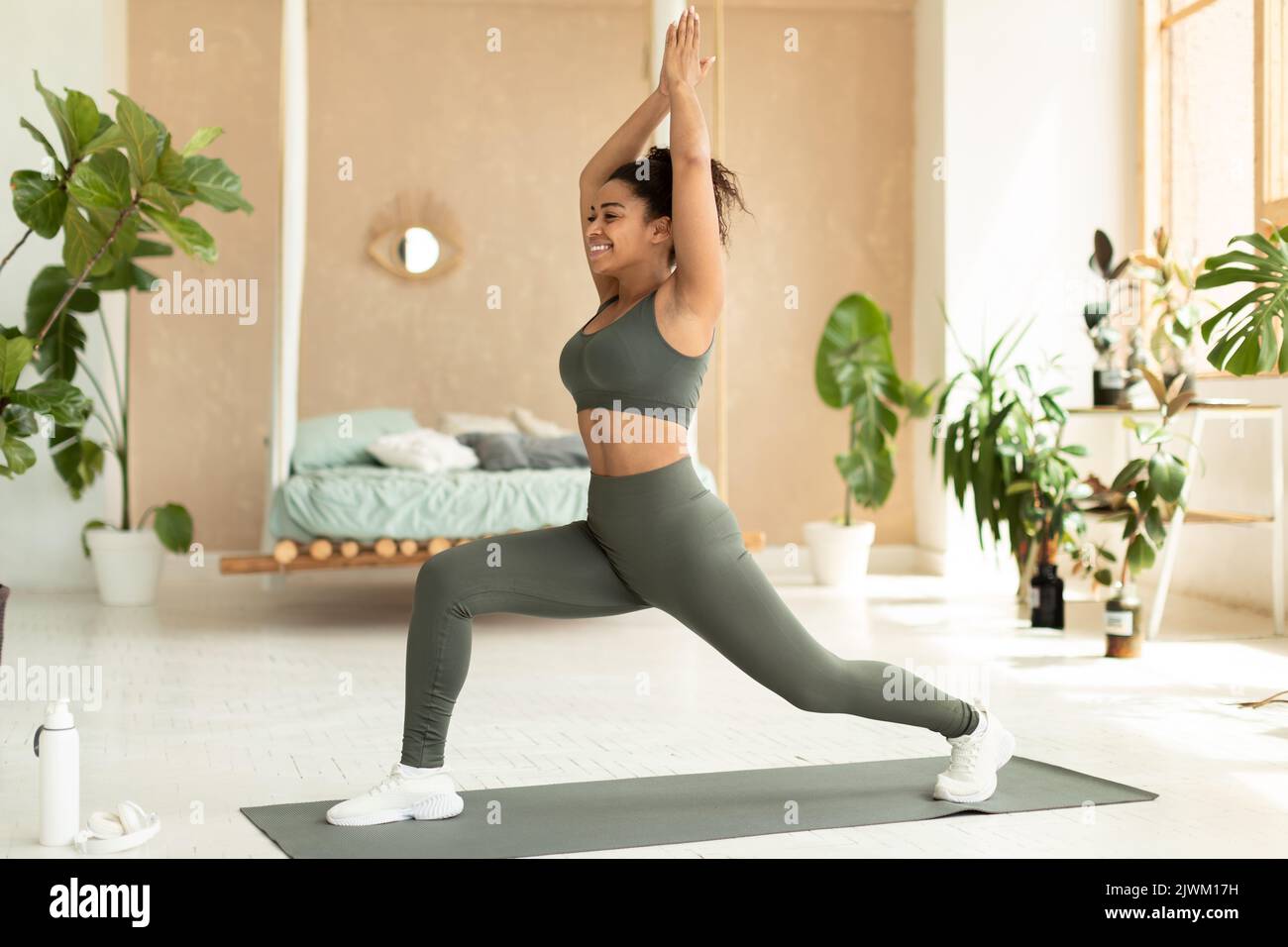 Entraînement de yoga domestique. Femme noire debout en 1 guerrier pose sur le tapis de sol, faisant des fentes avant, s'exerçant à la maison Banque D'Images