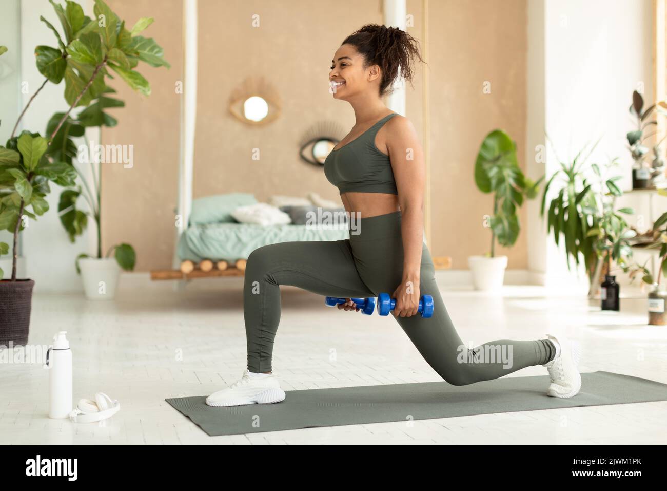 Concept d'entraînement de force. Femme afro-américaine sportive faisant des exercices de fente avec des haltères, s'entraîner à la maison Banque D'Images
