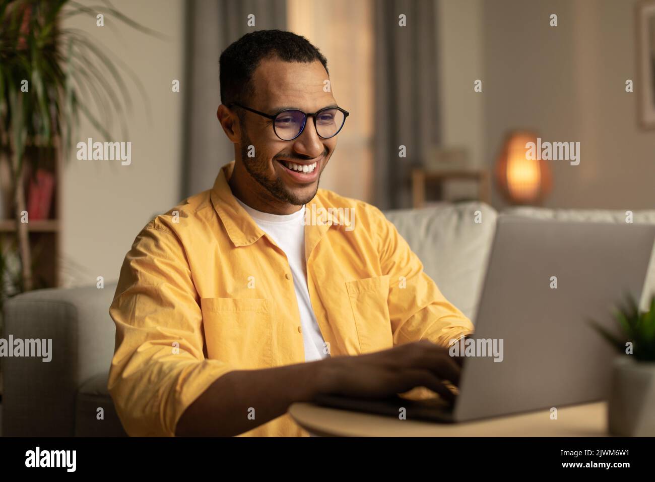 Beau jeune homme noir travaillant sur un PC portable, appréciant un travail à distance ou l'éducation dans le salon Banque D'Images