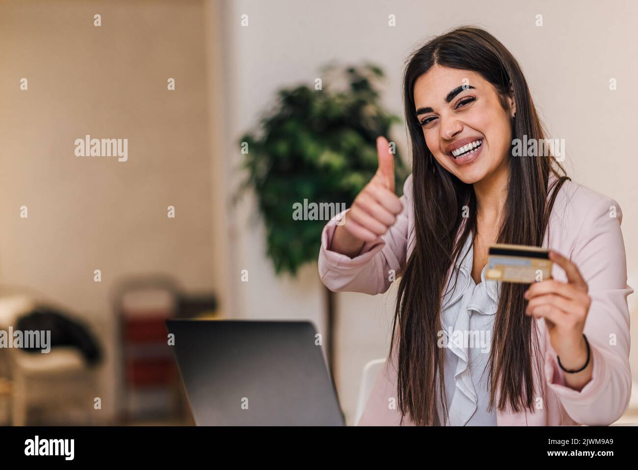 Jeune femme souriante, au bureau, heureuse avec les articles qu'elle a commandés en ligne en utilisant la carte de crédit. Banque D'Images