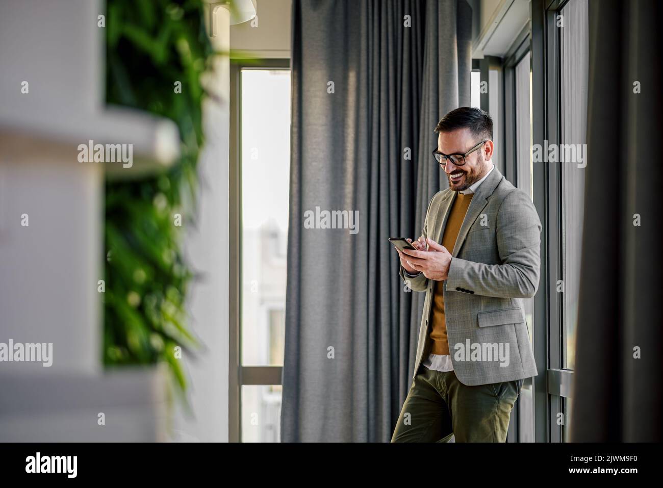 Surpris jeune homme d'affaires adulte, debout dans le hall, défilant dans son téléphone. Banque D'Images
