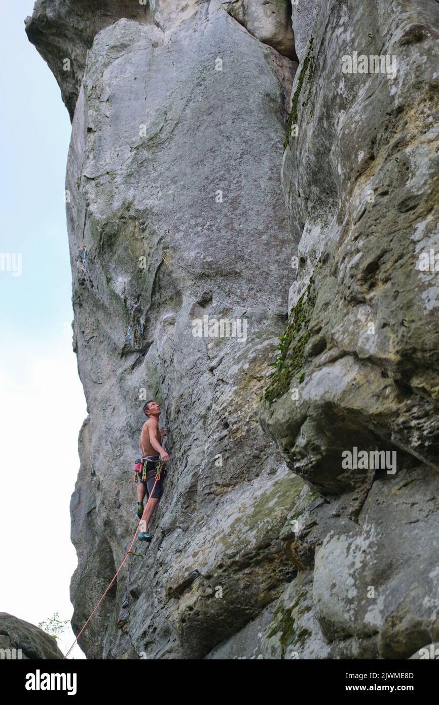 Grimpeur déterminé qui monte sur un mur escarpé de montagne rocheuse. Un sportif qui surmonte un itinéraire difficile. S'engager dans les sports extrêmes et l'escalade Banque D'Images
