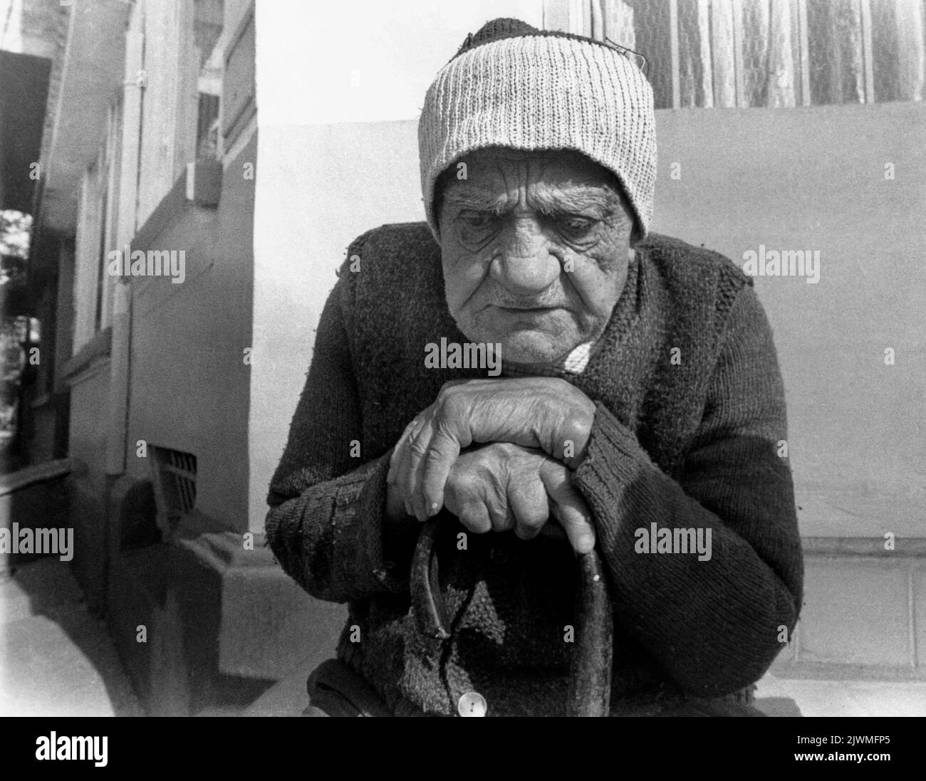 République socialiste de Roumanie, environ 1985. Homme âgé avec une canne assise à l'extérieur de sa maison, au soleil. Banque D'Images