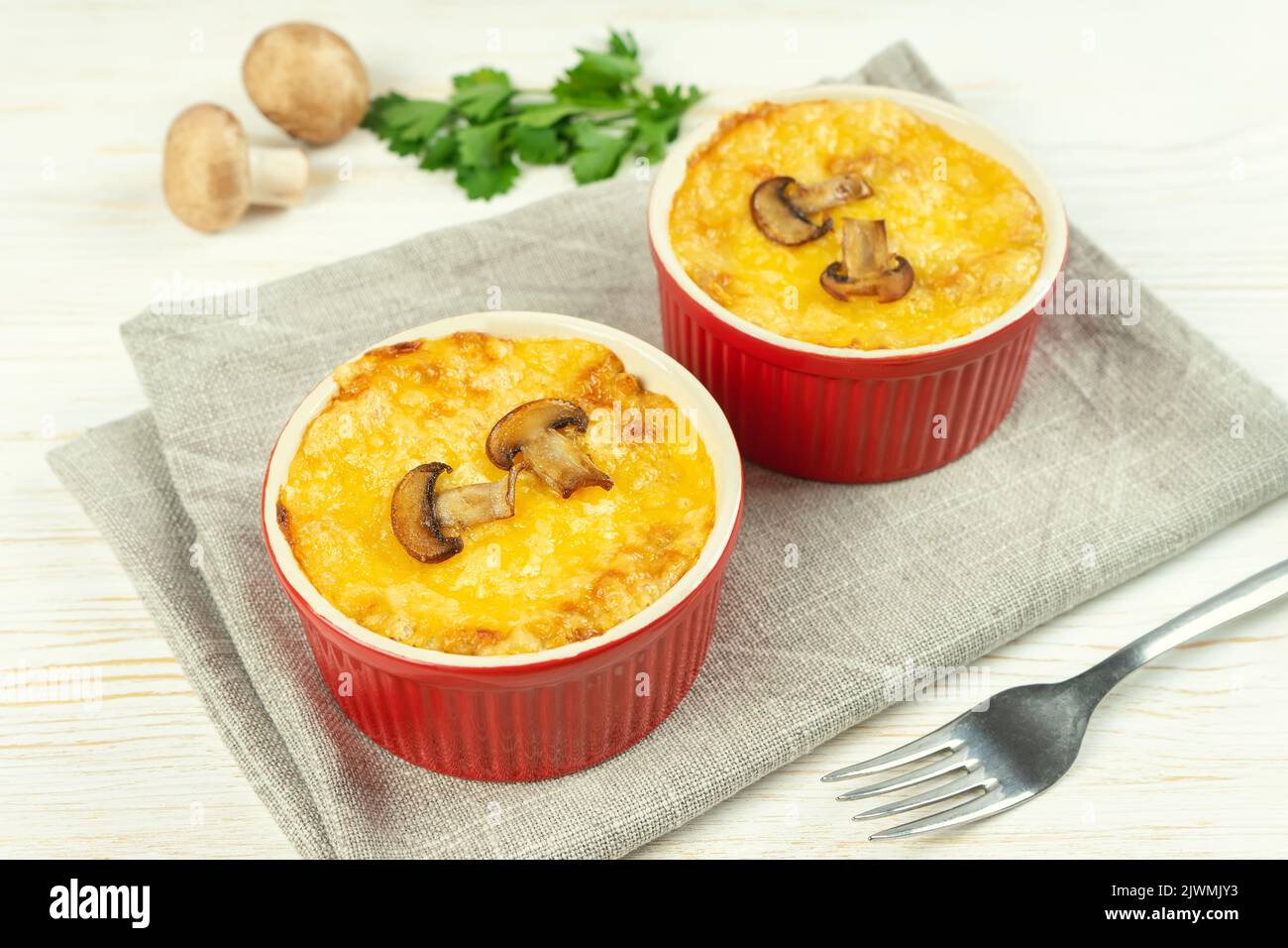 Cocotte de poulet et de champignons à la croûte dorée, julienne au fromage au four, gratin crémeux en portion de ramequin sur fond de bois blanc. FR Banque D'Images