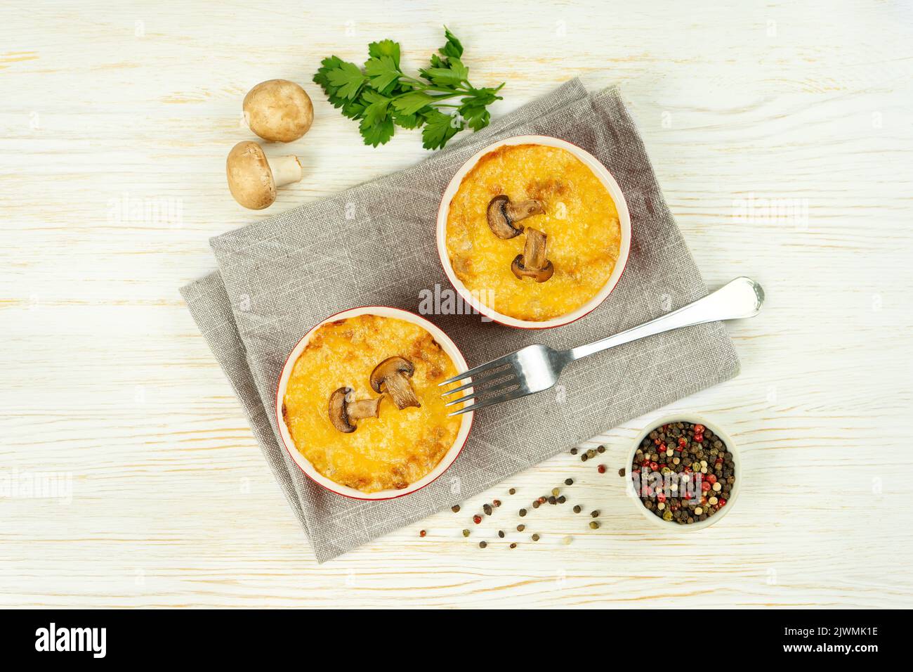 Cocotte de poulet et de champignons à la croûte dorée, julienne au fromage au four, gratin crémeux en portion de ramequin sur fond de bois blanc. FR Banque D'Images