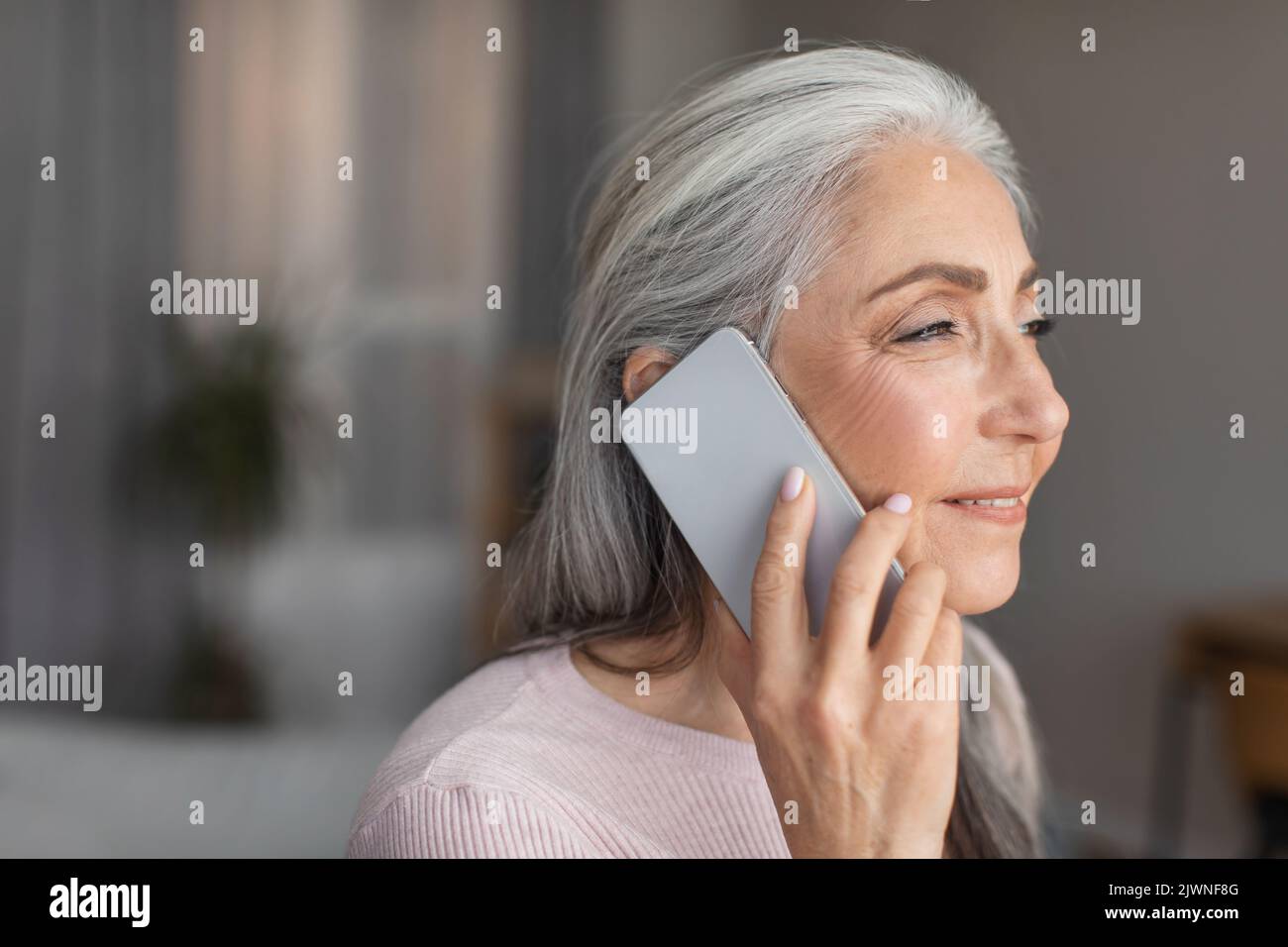 Souriante caucasienne mature gris-cheveux dame parlant par téléphone dans la chambre intérieur, profil, gros plan Banque D'Images