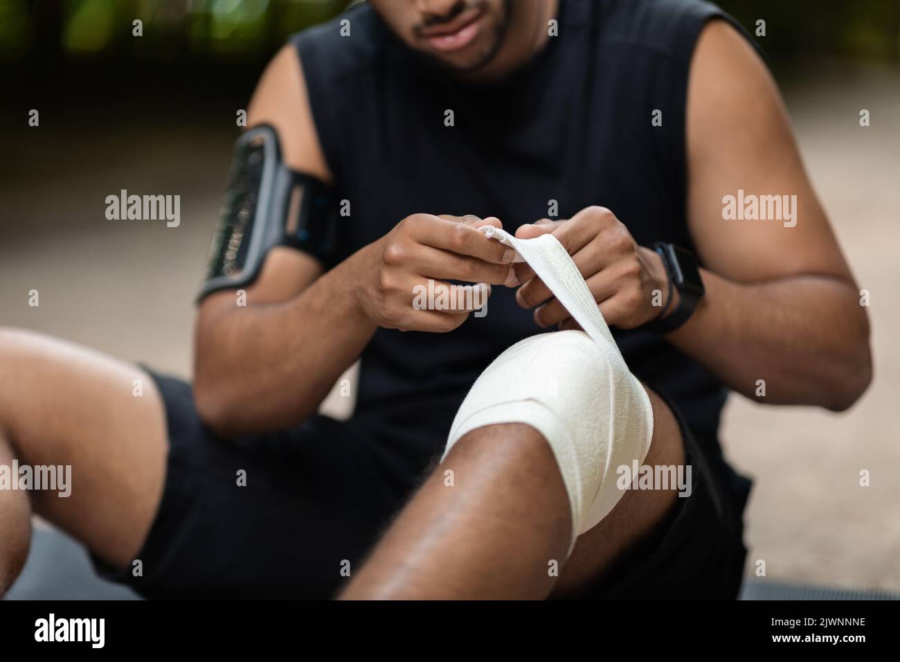 Écourté d'un athlète assis au sol, enroulant le genou blessé Banque D'Images