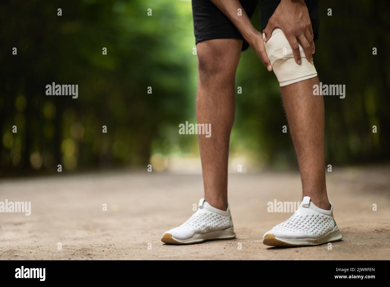 Un sportif méconnaissable enroule le genou blessé avec un bandage élastique Banque D'Images