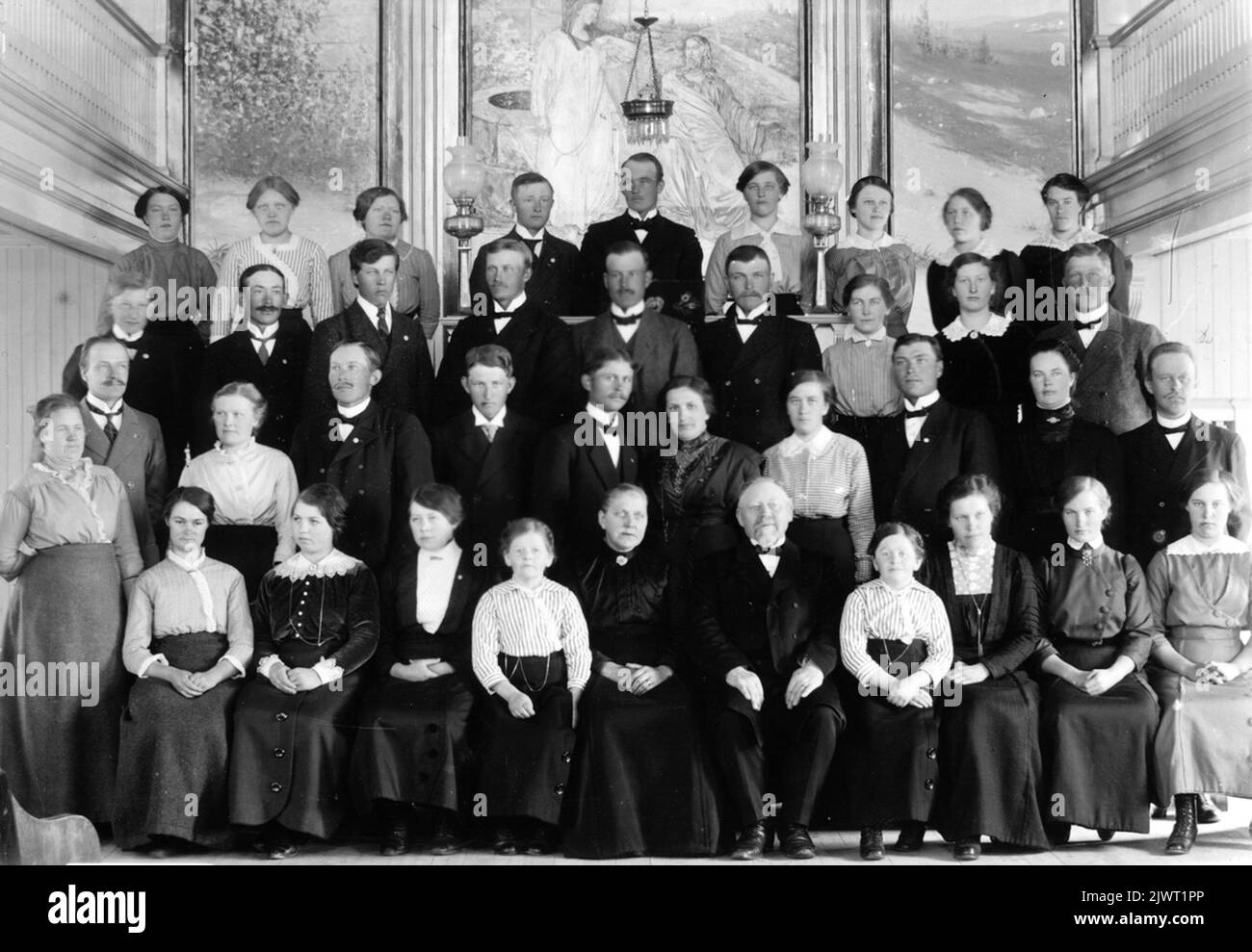 Maison de mission forestière. Le prédicateur Bäcklund avec sa femme se trouve dans la première ligne sous les numéros 5 et 6. Les numéros 4 et 7 sont 'Lill-Marta' et 'Lill-Anna' Stålberg. Ils sont restés petits toute leur vie. Debout dans la deuxième rangée à partir de la gauche, le maître de poste Jonas Kregatz et sa femme Ingeborg (fille du professeur d'école Engberg). Skogs missionshus. Pendikant Bäcklund med fru sitter i första raden som nummer 5 och 6. Nummer 4 och 7 är 'Lill-Marta' och 'Lill-Anna' Stålberg. De förblev små hela sitt liv. Stående i andra raden från vänster, postmästare Jonas Kregatz och hans fru Ingeborg (dotter till skollärare Engbe Banque D'Images