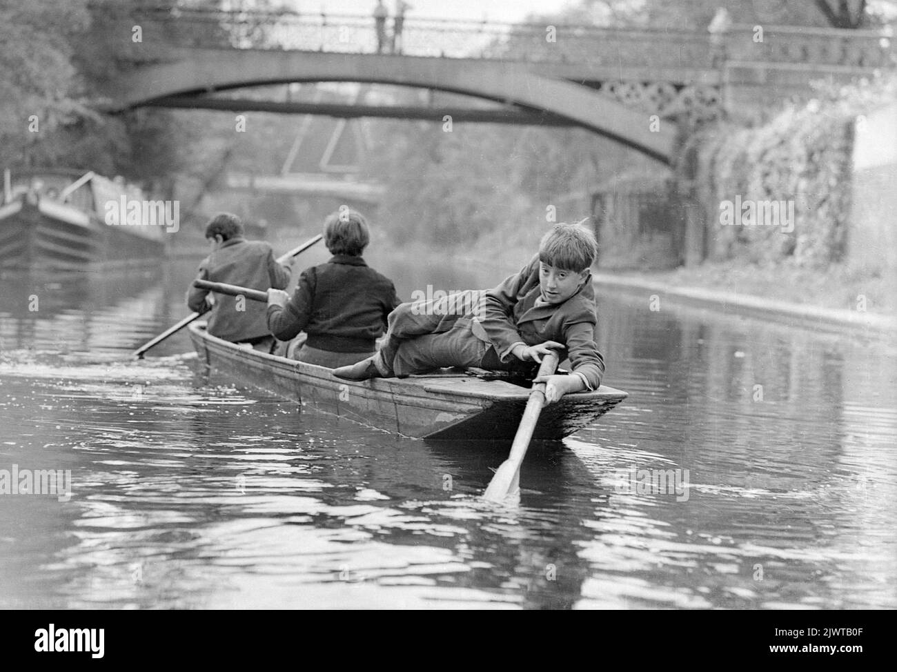 Londres, Angleterre, vers 1967. Trois garçons du Piratess’ Club pagayent un bateau le long du canal Regent’ près du bassin Cumberland. Au loin, vous apercevez une passerelle et le Snowdon Aviary du zoo de Londres dans Regent's Park. Le Piratess’ Club, un club de canotage pour enfants, a été créé en 1966 à Gilbey’s Wharf, sur le canal Regent's, près de Camden, à Londres. Leur pavillon était une ancienne barge et un certain nombre de petits bateaux et de canoës avaient été donnés pour les enfants. Banque D'Images