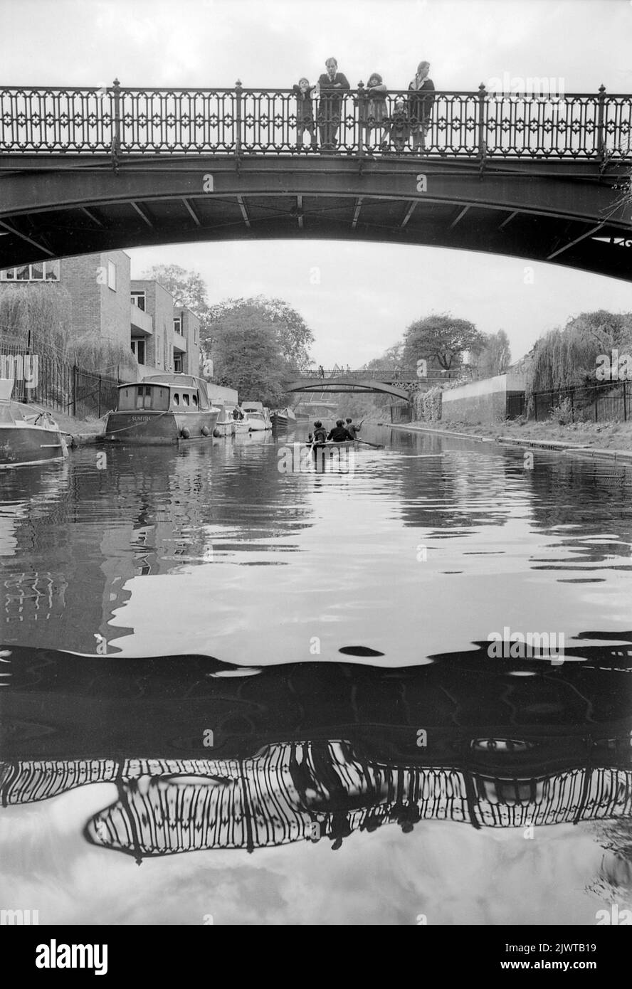 Londres, Angleterre, vers 1967. Une famille qui se tient sur la large passerelle au-dessus du canal Regent’ à Cumberland Basin observe des garçons du Pirates Club pagayer un bateau en dessous d’eux. Le Snowdon Aviary du zoo de Londres se trouve à l'avant de l'hôtel, à Regent's Park. Le Piratess’ Club, un club de canotage pour enfants, a été créé en 1966 à Gilbey’s Wharf, sur le canal Regent's, près de Camden, à Londres. Leur pavillon était une ancienne barge et un certain nombre de petits bateaux et de canoës avaient été donnés pour les enfants. Banque D'Images