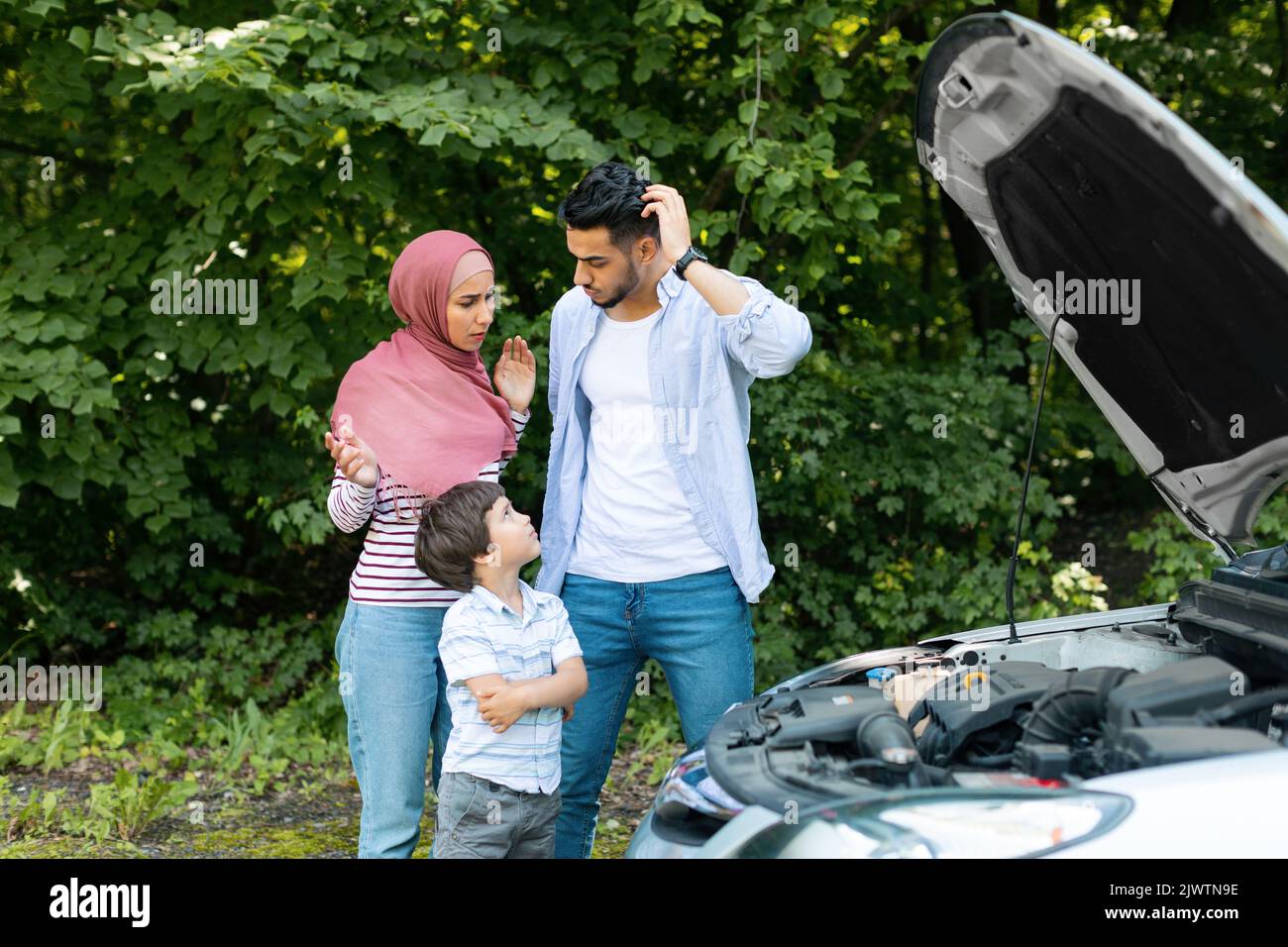 Triste déception millénaire mari et femme islamique dans hijab avec stand d'enfant près de la voiture cassée avec le capot ouvert Banque D'Images