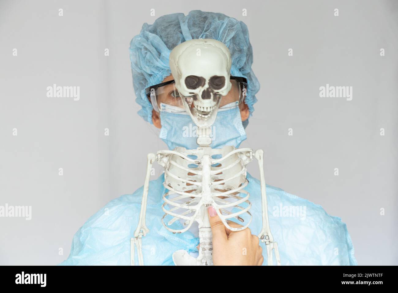 Fille médecin dans un manteau avec des lunettes et un masque et un squelette sur un fond isolé, un médecin dans un costume médical, la médecine Banque D'Images