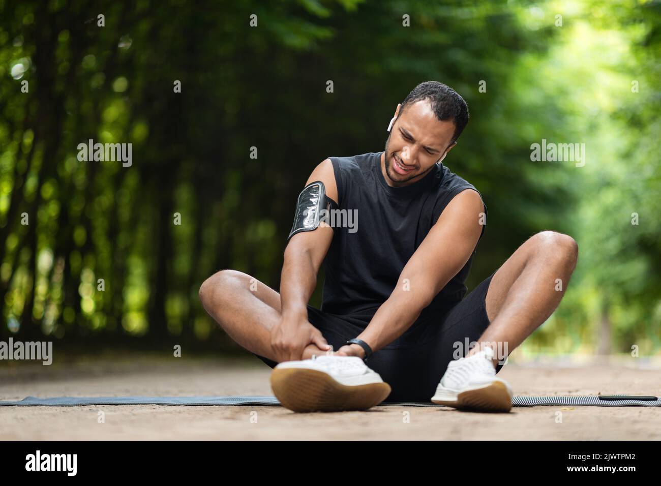 Beau sportif noir s'exerçant dans un parc public, touchant la cheville Banque D'Images